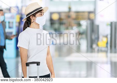 Young Female Wearing Face Mask With Luggage Checking Flight Time In Airport, Protection Coronavirus 