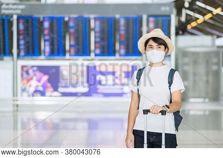 Young Female Wearing Face Mask With Luggage Checking Flight Time In Airport, Protection Coronavirus 