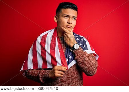 Young handsome latin patriotic man wearing united states of america falg serious face thinking about question, very confused idea