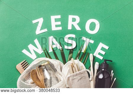 Zero waste concept. Cotton bag, bamboo cultery, glass jar,  bamboo toothbrushes, hairbrush and straws on green background, flat lay, paper text , copyspace. Sustainable lifestyle concept.