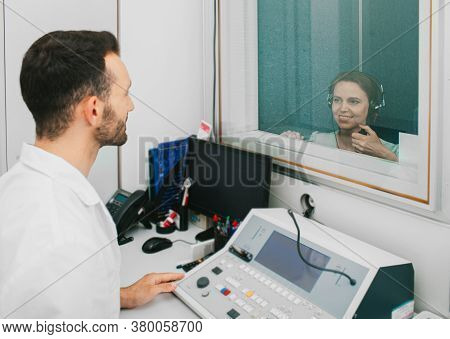 Audiologist Man Doing The Hearing Exam To An Adult Woman Patient Using An Audiometer In A Special Au