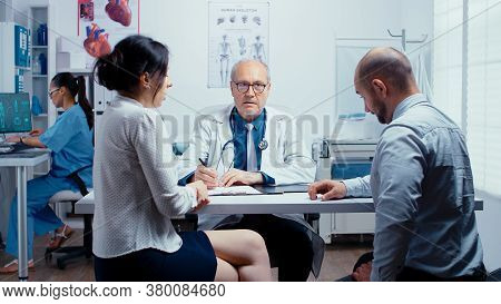 Young Couple Talking With Senior Doctor In Modern Private Clinic. Family Planning Specialist. People