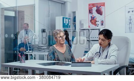 Doctor Filling Out Prescription On Digital Tablet While Consulting Elderly Senior Retired Woman. Hea