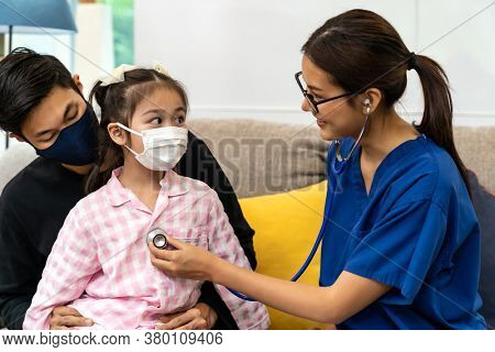 Asian female doctor use stethoscope to listen heartbeat of little girl child sit with her father in living room while doctor visit at home. Home health care delivery and doctor visiting concept.