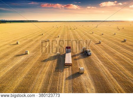 Aerial View Of Truck With Hay Bales. Agricultural Machinery. Chamfered Field And Hay Stacks After Ha