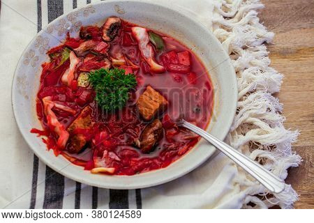 Closeup On Spoon Getting A Piece Of Red Meat From Borscht Soup In Tan Bowl On Tan Dishcloth Over Woo