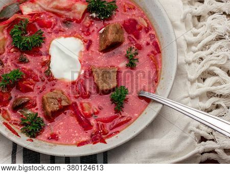 Closeup On Spoon Getting A Piece Of Red Meat From Borscht Soup In Tan Bowl On Tan Dishcloth