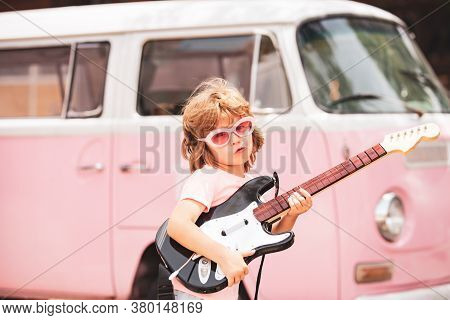 Kid Musician Playing The Guitar Like A Rockstar On Pink Background In Neon Light. Cute Pupil Having 