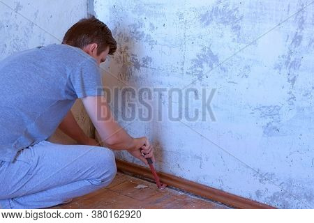 Man Workman Making Renovation, Removing Plinth From Old Wall And Floor Using Crowbar. Construction W