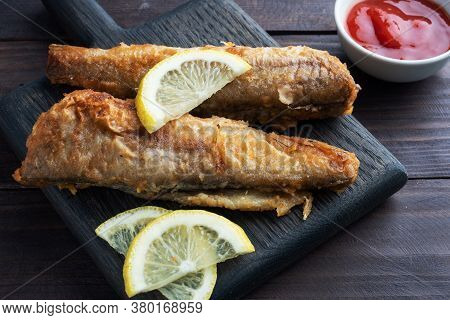 Fried Fish Hake Pollock With Tomato Sauce And Slices Of Fresh Lemon. Concept Eating Fatty Fast Food.