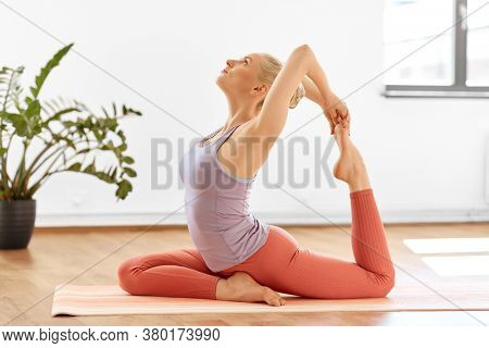 fitness, sport and healthy lifestyle concept - young woman doing mermaid pose at yoga studio