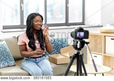 blogging, videoblog and people concept - happy smiling african american female beauty blogger with camera and perfume videoblogging at home