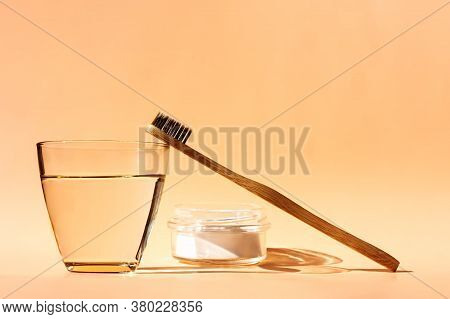 Bamboo Toothbrush, Glass Of Water And Toothpaste Powder On A Peach-colored Pastel Background. Biodeg