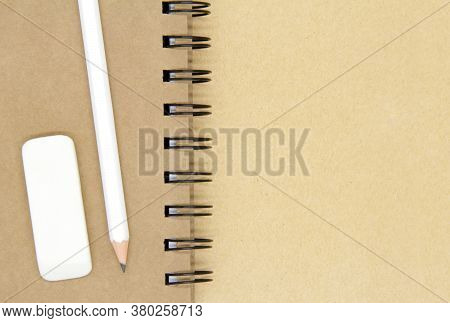 Kraft Notepad, White Pencil, White Eraser On A Brown Craft Background. Notebook, Eraser And Pencil O