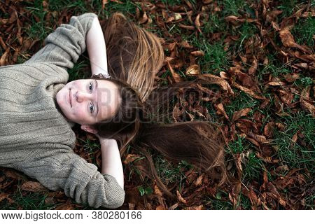Teengirl laying on autumn ground with long hair scattered on grass.