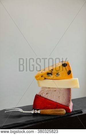 Different Types Of Delicious Cheeses And Fork On Slate Plate