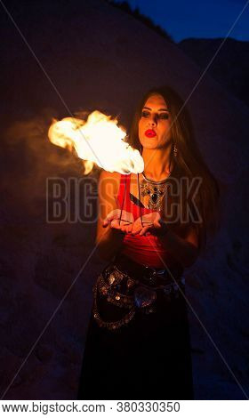 Young Long-haired Woman In A Red Top And Ethnic Necklace Holds On Handbreadth Two Small Torch And Bl