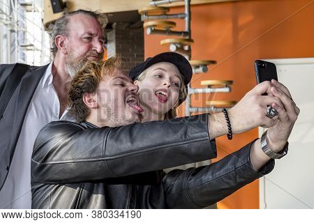 Kiev, Ukraine, 03.23.2020: Selfies Are Made By Two Men And A Girl. The Couple Sticks Out Their Tongu