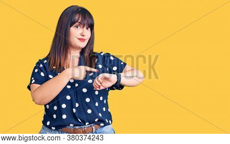 Young plus size woman wearing casual clothes in hurry pointing to watch time, impatience, upset and angry for deadline delay 