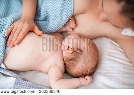 Happy Young Woman Feeds Breast Milk And Hugs Baby. A Mother Is Breastfeeding A Newborn Baby While Ly