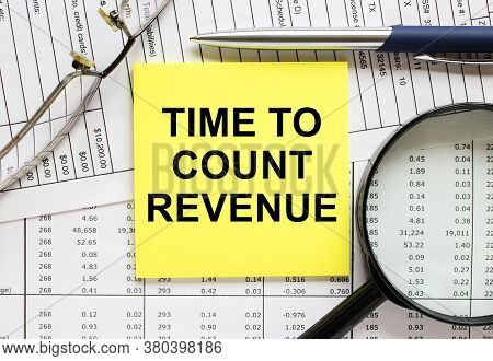 Text Time To Count Revenue On Financial Tables With Pen, Glasses And Paper Clips