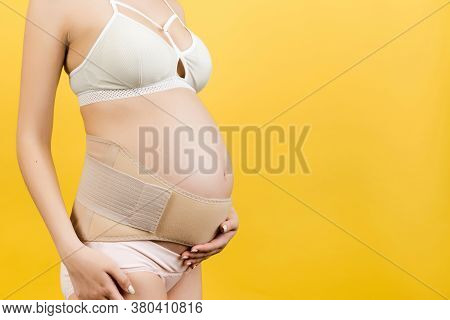 Side View Of Pregnant Woman In Underwear Wearing Pregnancy Bandage At Yellow Background With Copy Sp