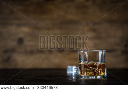 Whisky, Whiskey, Bourbon Or Cognac With Ice Cudes On Black Stone Table And Wood Background