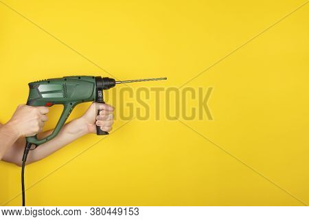 Green Puncher In The Hands Of A Builder. Male Hands Hold New Puncher Or Drill Isolated On Yellow Bac