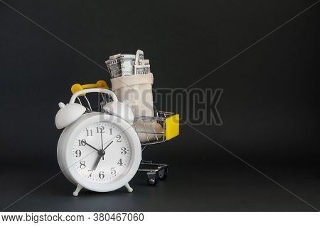 A White Alarm Clock And Shopping Basket With A Canvas Bag Full Of Money On A Dark Isolated Backgroun