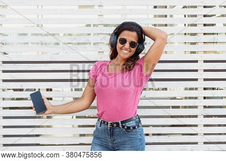 Young Women Listening Music With Headphones From Smartphone Near A Wall