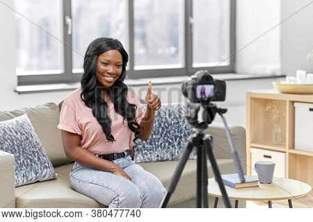 blogging, videoblog and people concept - happy smiling african american female video blogger with camera videoblogging at home and showing thumbs up