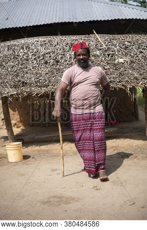An African Older Man In Red Muslim Taqiyyah Fez Hat Posing With A Stick For Lame People On Yard Near