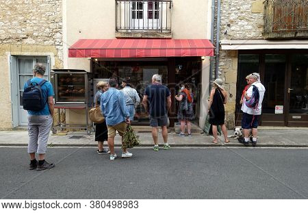 Monpazier, France July 2020: Customers Queing Outside A Butchers In A French Town With Numbers Insid