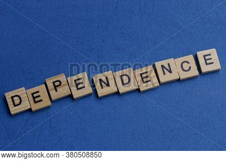Word Dependence Made From Gray Wooden Letters Lies On A Blue Table