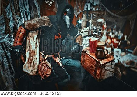 The plague doctor is working at his desk, inventing a cure for bubonic plague. The atmosphere of mysticism. Historical reenactment. Halloween. 