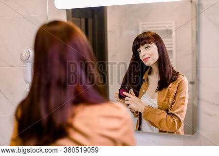 Back View Of Beautiful Young Woman In White Undershirt And Yello Shirt, Combing Her Dark Red Straigh