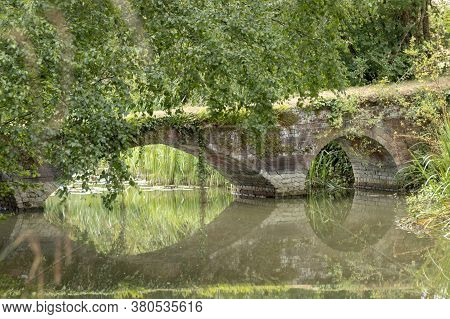 A Close Up View Of A Brick Bridge That Is Crossing Over The Lake Or Pond And Has The Reflection Of T