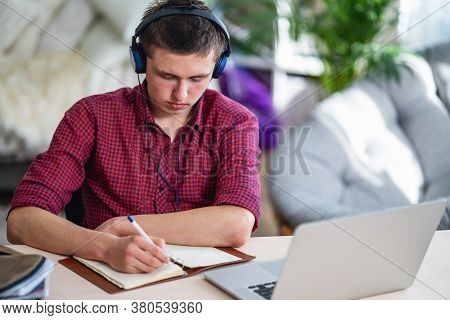 Brooding Active Teen Guy With Headphones Listens To Lecture, Does In Notebook, Using Laptop And Make