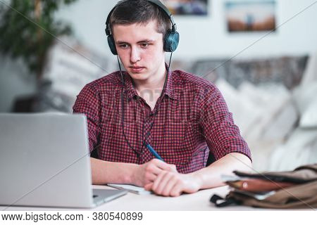 Brooding Active Teen Guy With Headphones Listens To Lecture, Does In Notebook, Using Laptop And Make