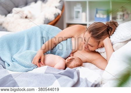 Happy Young Woman Feeds Breast Milk And Hugs Baby. A Mother Is Breastfeeding A Newborn Baby While Ly