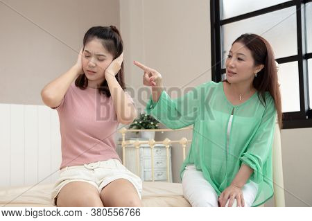 Annoyed Asian Teen Girl Sitting On Bed With Closes Her Ears With Her Hands Does Not Listening To Her