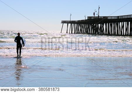 Auguast 3, 2020 In Pismo Beach, Ca:  Surfer Walking Into The Ocean Carrying His Surfboard Taken In P