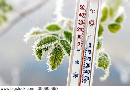 A Thermometer On A Background Of Frost-covered Leaves Shows 5 Degrees Below Zero