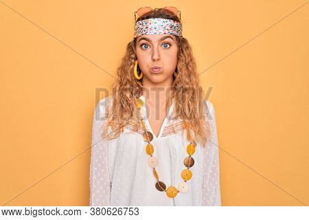 Young beautiful blonde hippie woman with blue eyes wearing sunglasses and accessories puffing cheeks with funny face. Mouth inflated with air, crazy expression.