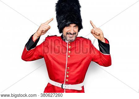 Middle age handsome wales guard man wearing traditional uniform over white background smiling pointing to head with both hands finger, great idea or thought, good memory