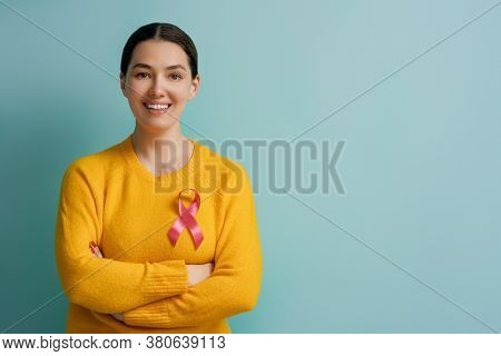Young woman on color turquoise background. Pink ribbon like a symbol of breast cancer awareness. Support people living with tumor illness.
