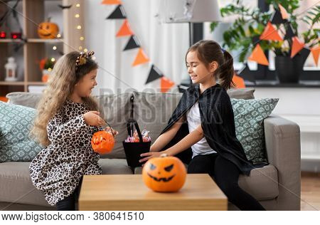 halloween, holiday and childhood concept - smiling little girls in costumes with candies at home