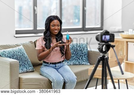blogging, videoblog and people concept - happy smiling african american female beauty blogger with camera and cosmetics videoblogging at home
