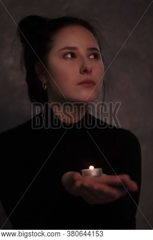 Dark Portrait Of A Sad Brunette Girl Almost Burst Into Tears In A Black Turtleneck Holding Candle Ag