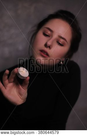 Dark Portrait Of A Sad Brunette Girl Almost Burst Into Tears In A Black Turtleneck Holding Candle Ag